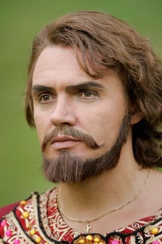 Costume portrait as Nabucco: dark beard and embroidered royal collar, outdoor light.