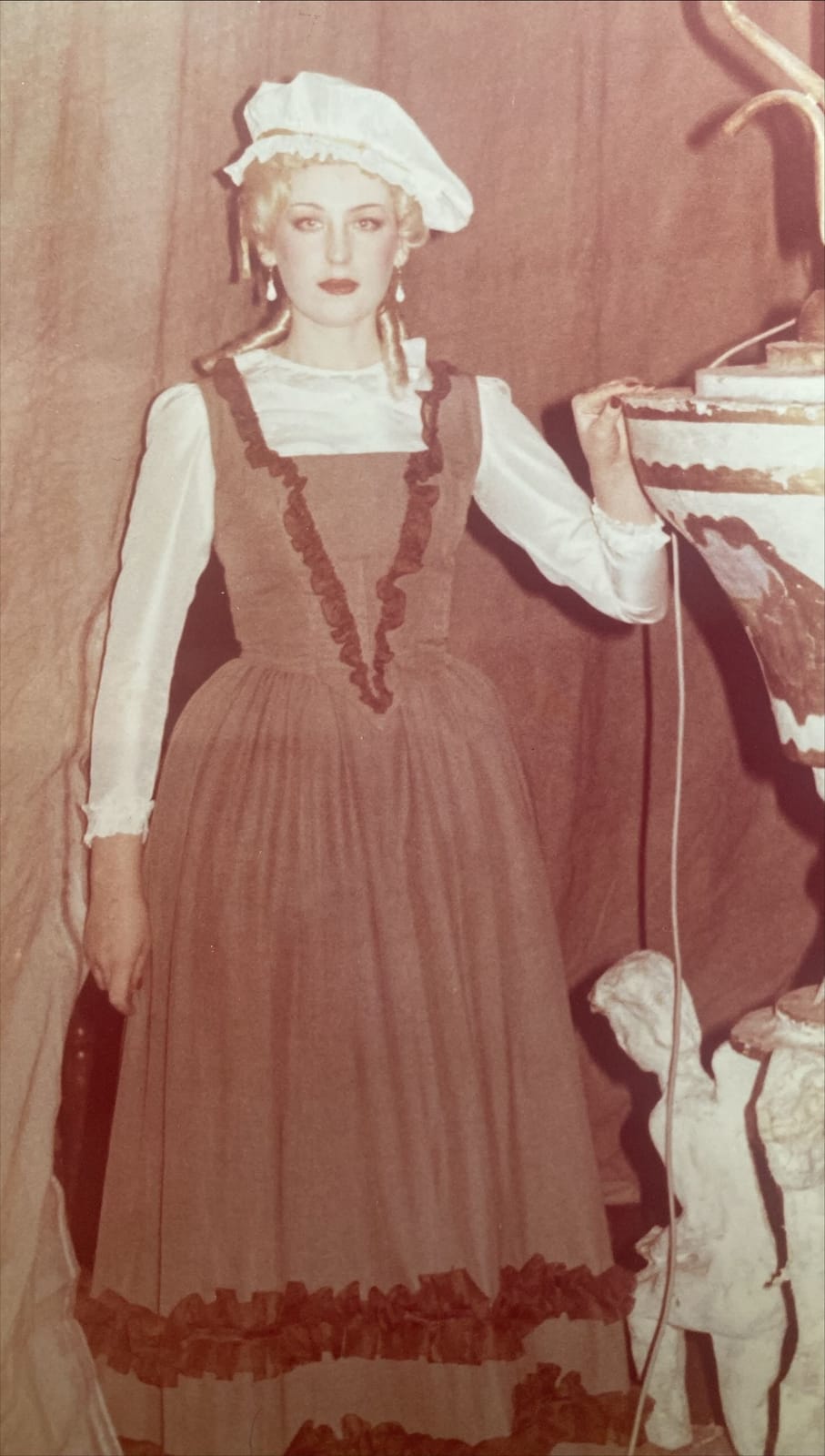 Archival role photograph: period maid costume with a white bonnet and rust-coloured dress.