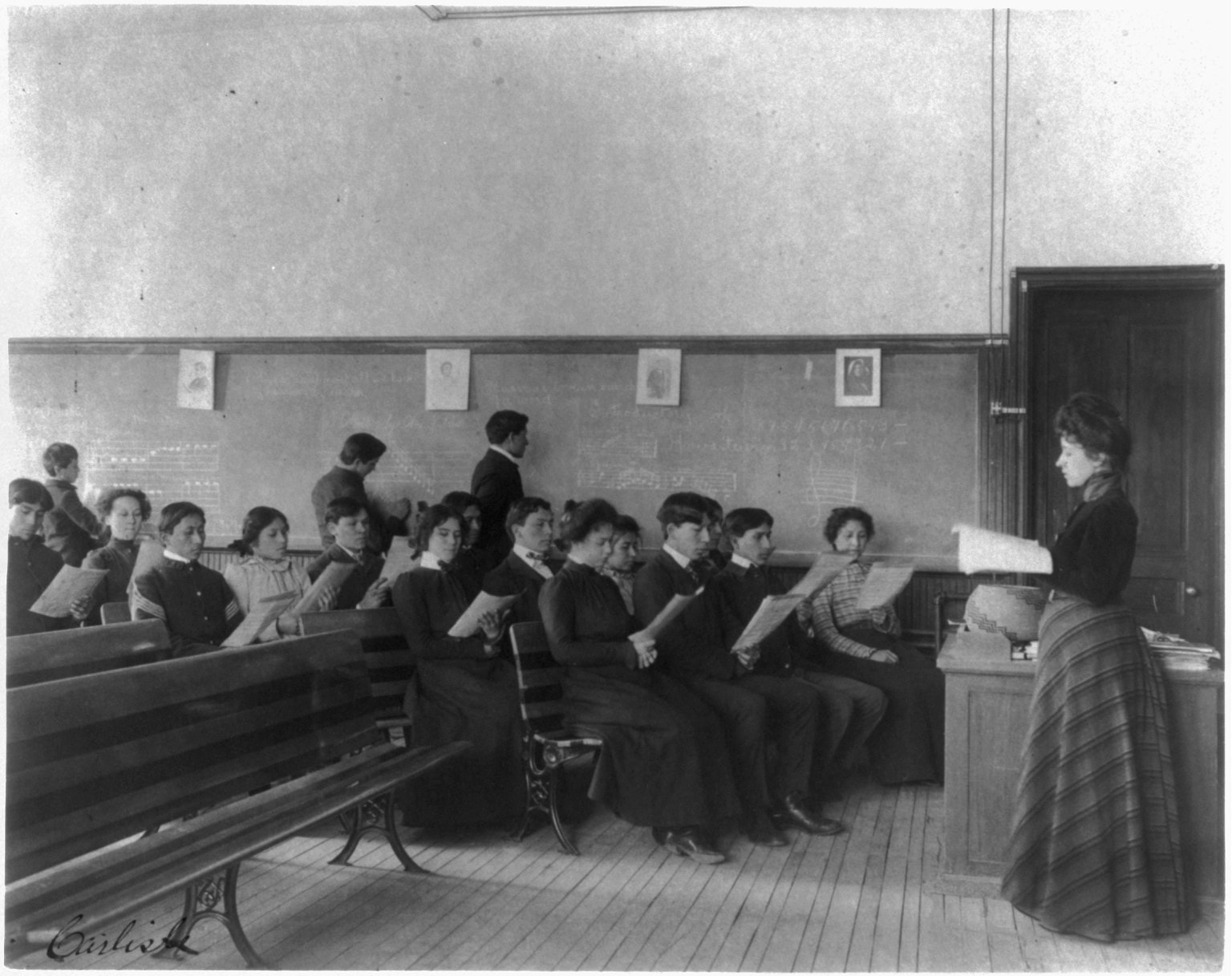 Historic photograph of a music class in 1901: students with violins and sheet music in a classroom.