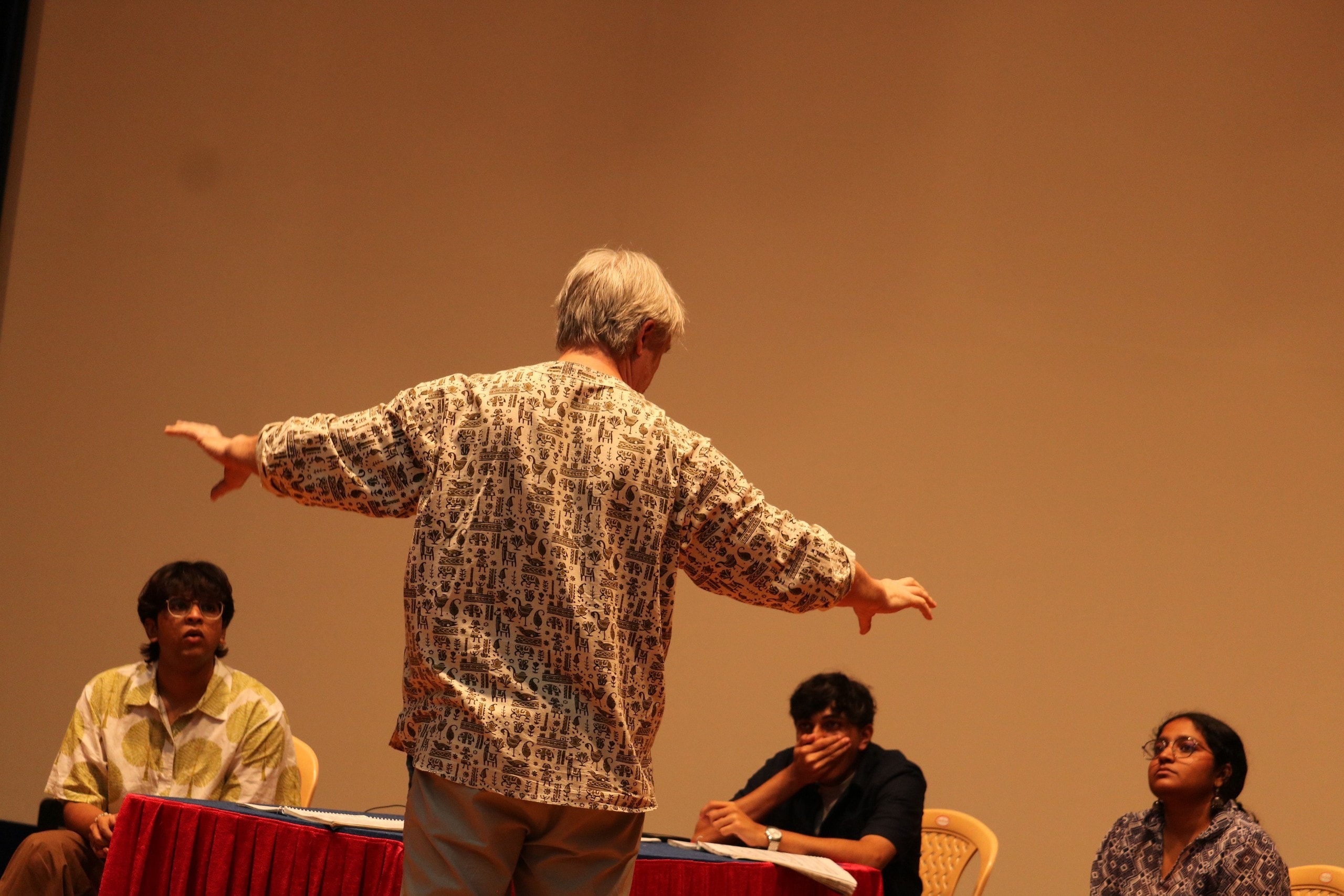 A staging rehearsal in progress: the director gives instructions to students seated with scripts.