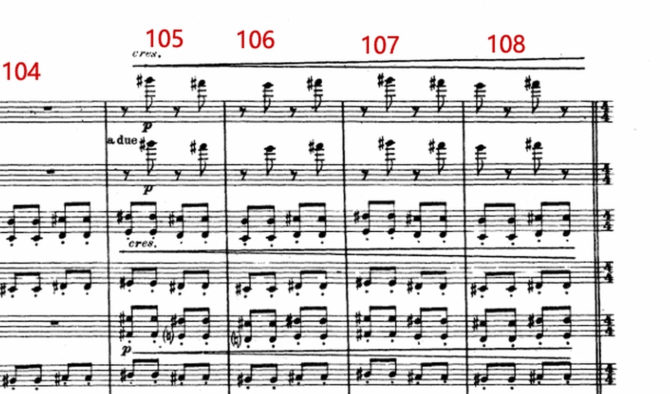 Close-up of a printed orchestral score marked with large red bar numbers.