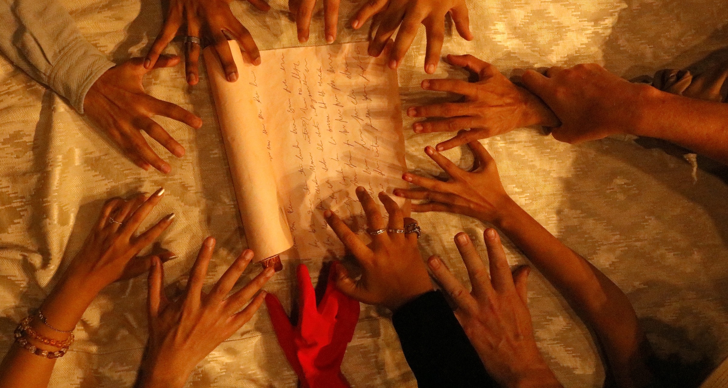 A scroll of the will on a table, many hands reaching for it in warm light.