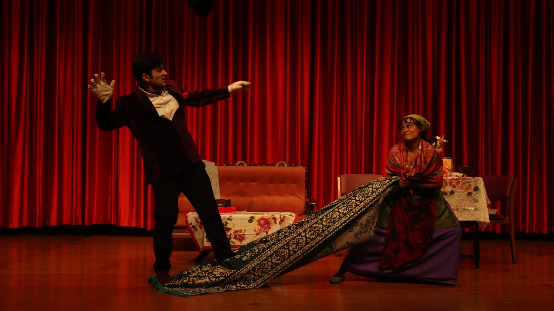 Scene from The Proposal: a man gestures as a woman drags a long carpet across the stage
