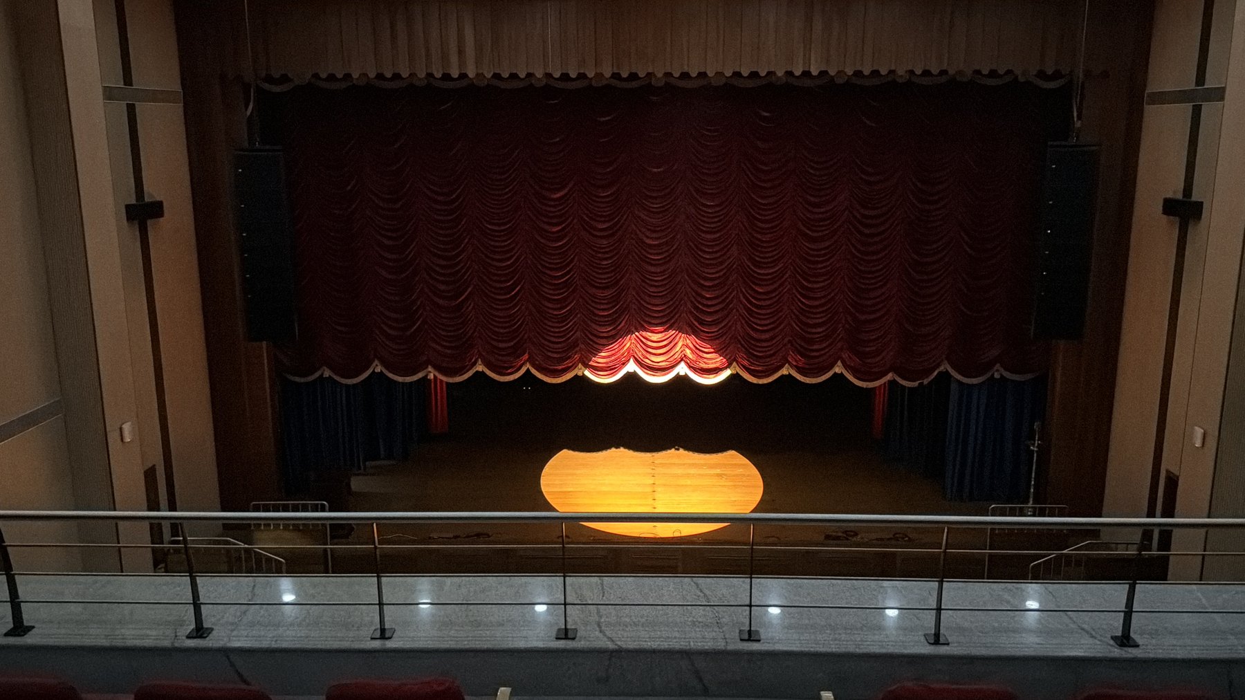 The empty KE Auditorium stage with a single pool of light and the curtain half open.