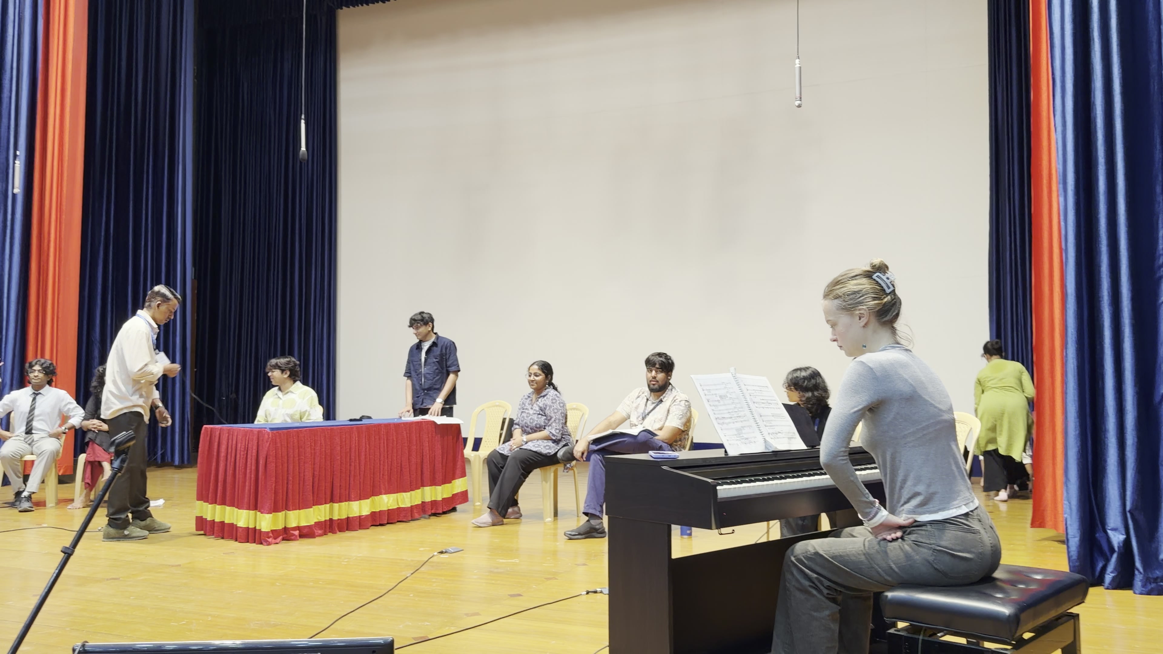 Anastasiya Yafimava at the piano on the KE Auditorium stage, the cast standing in a row behind her.