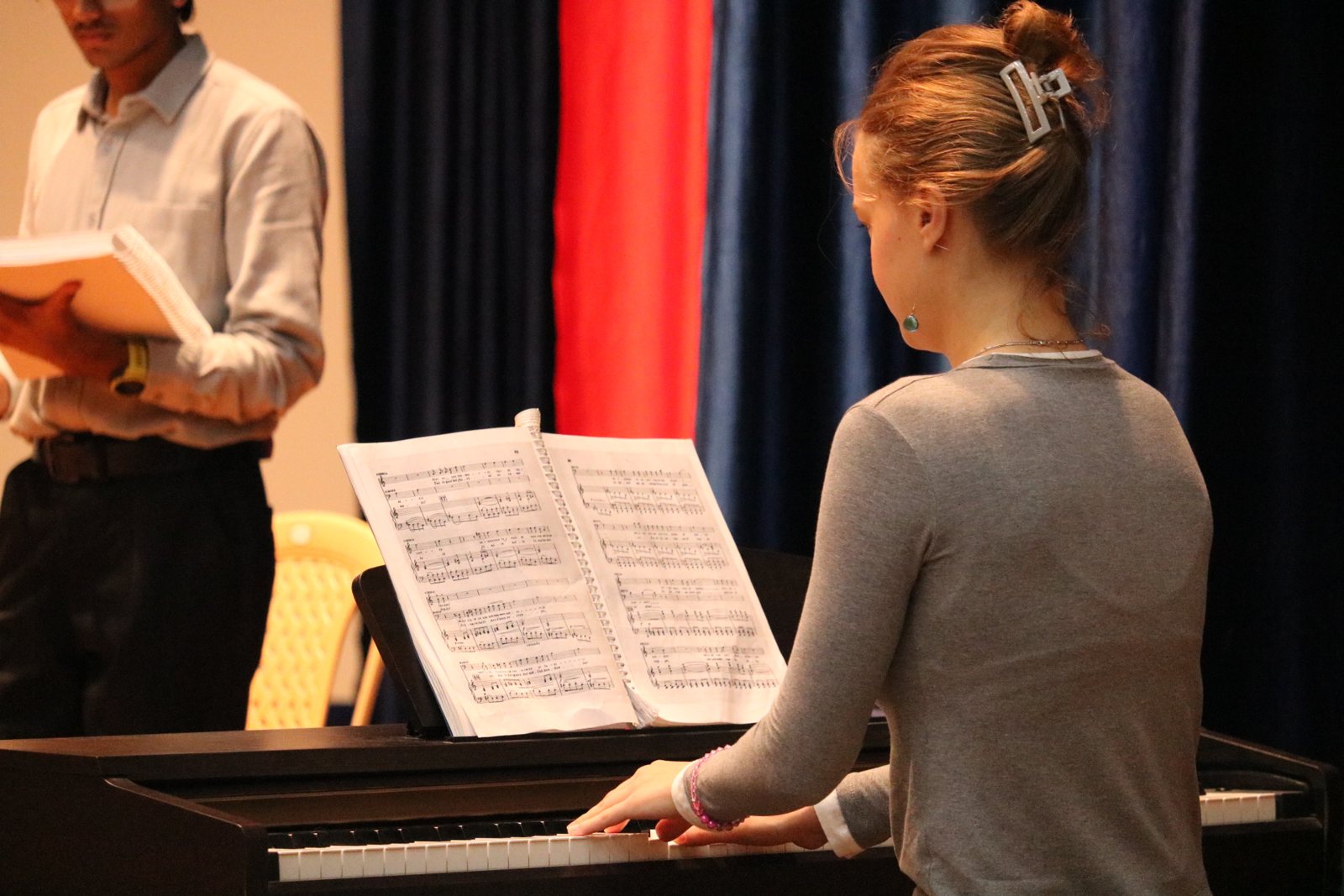 A repetiteur at the piano with the score open, a singer standing behind with his own copy.